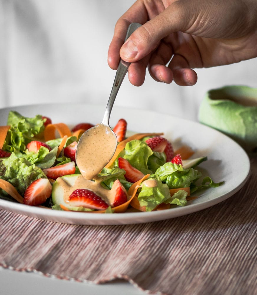 A photo of strawberry vinaigrette being spooned of a simple fresh salad of lettuce, slivered carrot and strawberries.