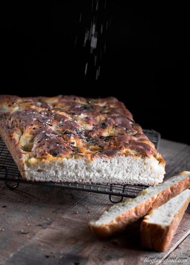 A photo of focaccia bread on a cooling wire rack with rosemary and sea salt on top. 