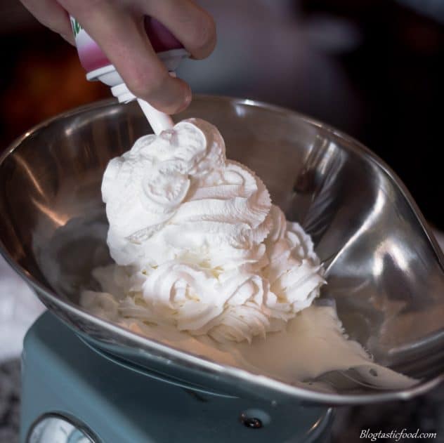 Cool whip being sprayed into a metal bowl on a weighing machine.