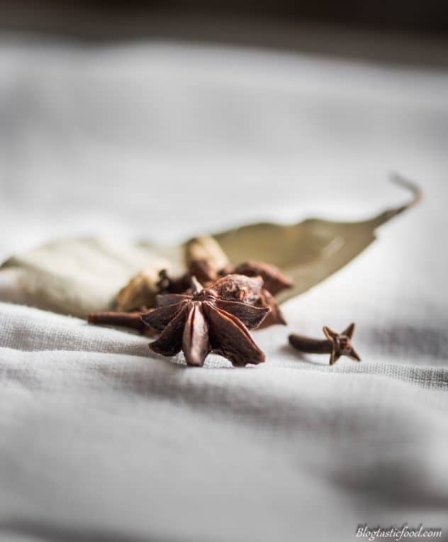 A couple of star anise, some cloves, some cardamom pods and a bay leaf on some white cloth.