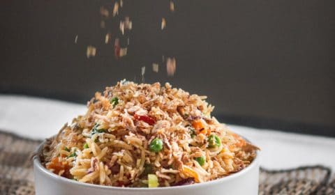 Some crispy fried shallots being sprinkled over a big bowl of fried rice,