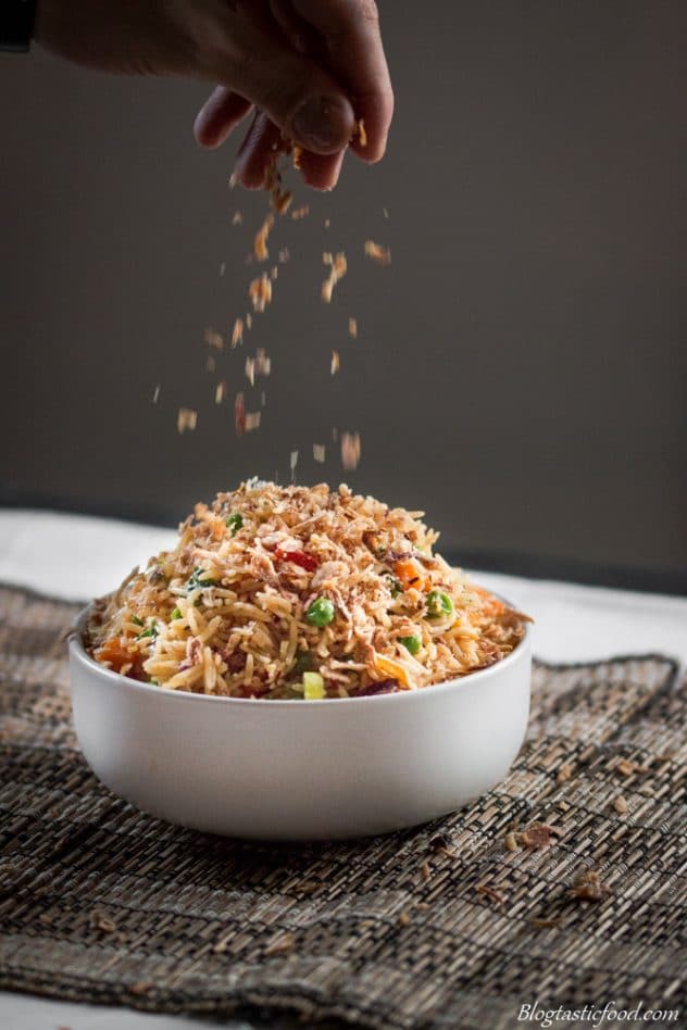 Some crispy fried shallots being sprinkled over a big bowl of fried rice,