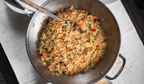 An overhead photo of fried rice in a wok surround by plates ready to be served.