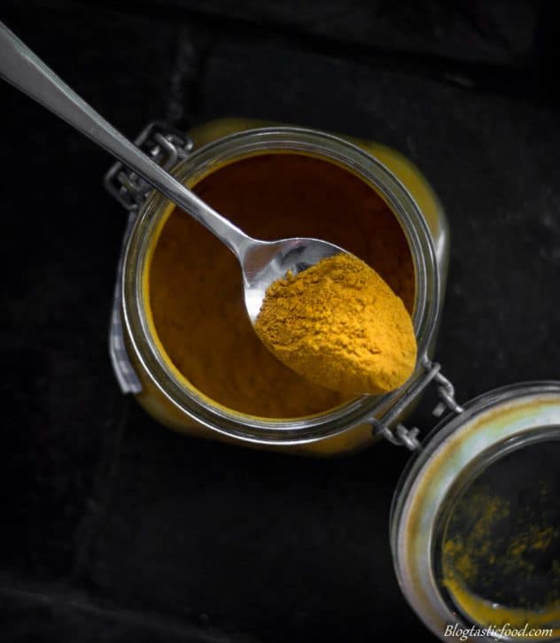 A photo of turmeric powder in a spoon and in a jar.