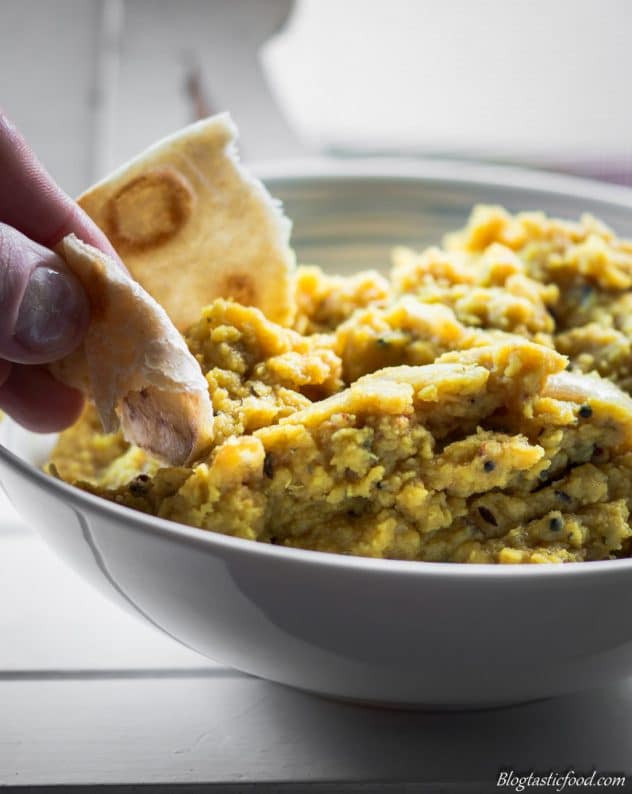 Someone dipping a piece of bread in a bowl of red lentil dhal.