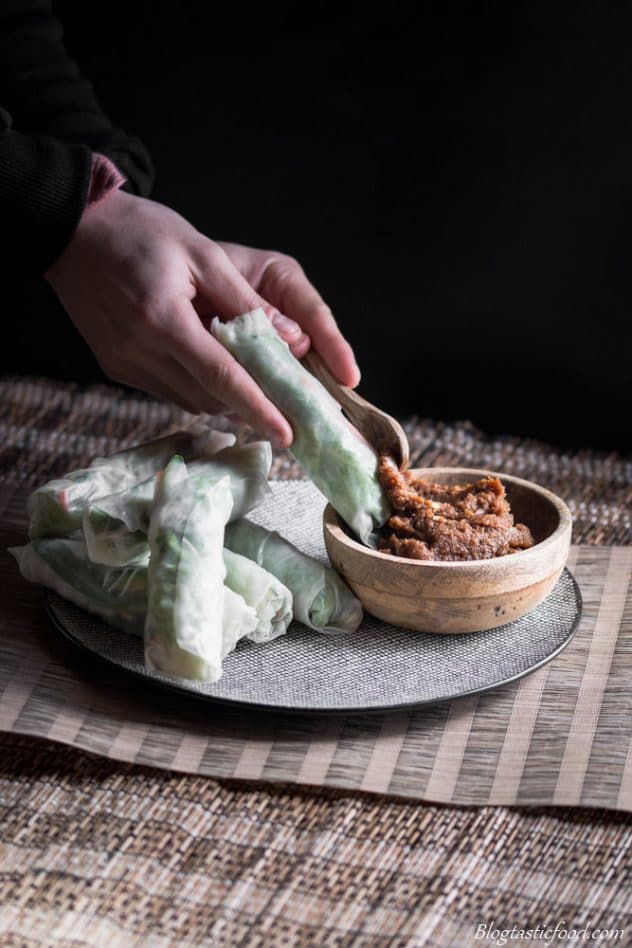 A photo of fresh Vietnamese spring rolls on a fancy plate with a small wooden bowl filled with peanut satay sauce on the side.