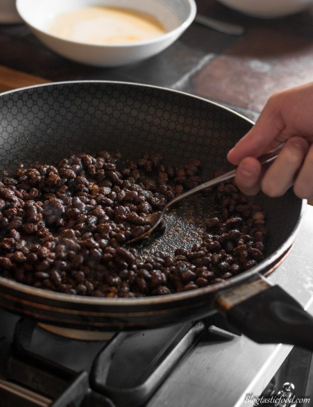 A photo of black beans being fried off in a pan.