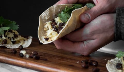 Some holding a soft shell taco filled with spiced black beans.