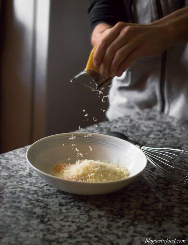 A photo of someone grating some parmesan cheese in a bowl filled with eggs. 