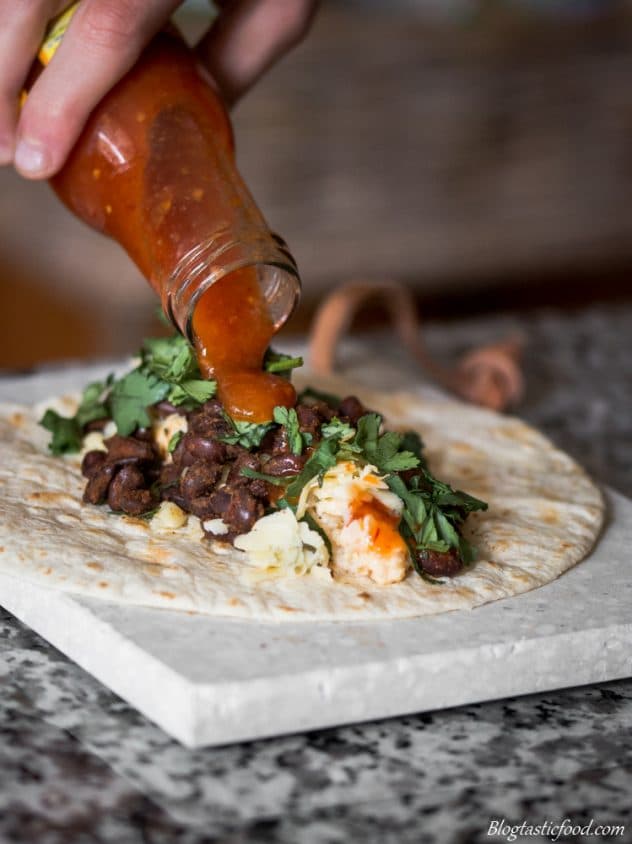 Habanero sauce being poured over a black bean taco.