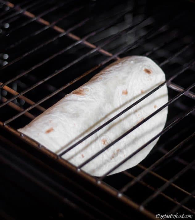 A plain tortilla draped over the bars of an oven rack.