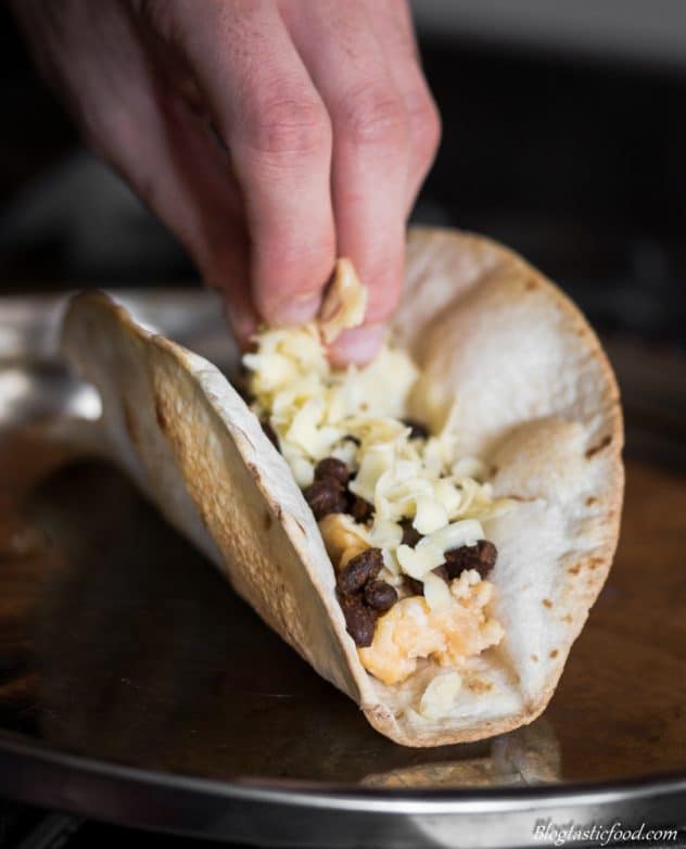 A photo of cheese being sprinkled over a black bean breakfast taco. 