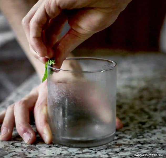 Someone rubbing fresh mint leaves around the rim of a glass.