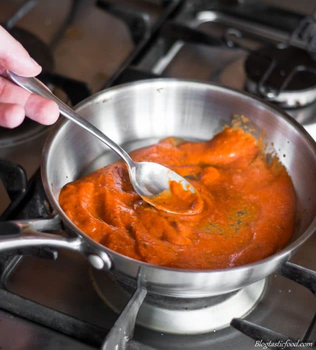 Someone stirring red pepper and tomato sauce on a pan. 