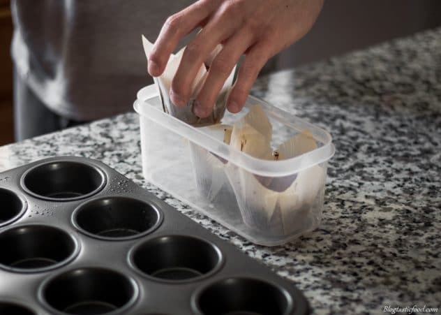 A photo og someone placing muffins in a container. 