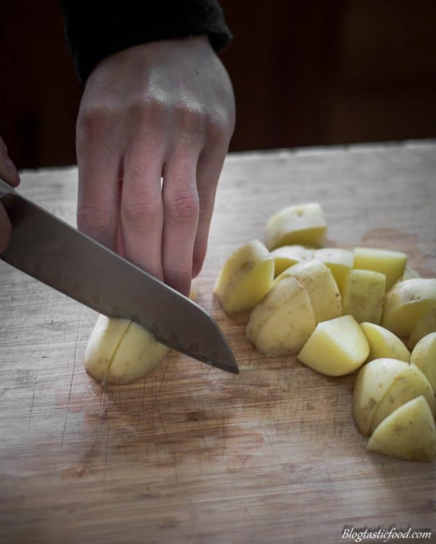 Someone cutting potatoes about an inch thick on a chopping board.