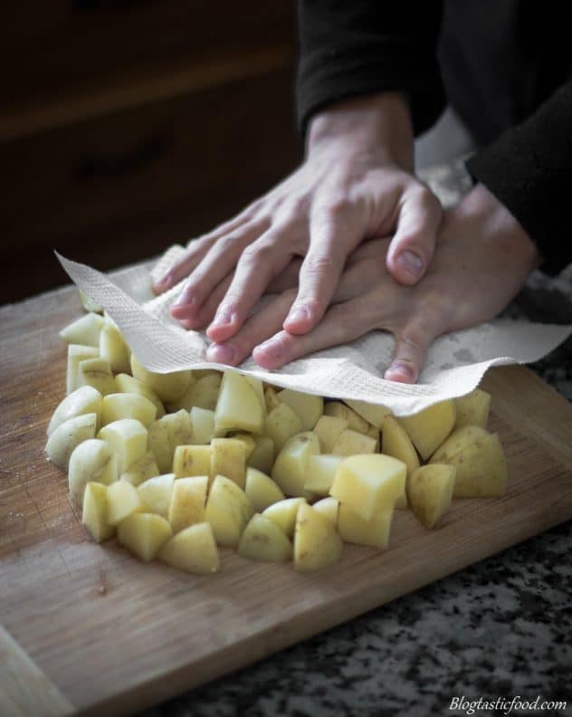 A photo of some using kitchen paper to soak up the moisture of diced potatoes.