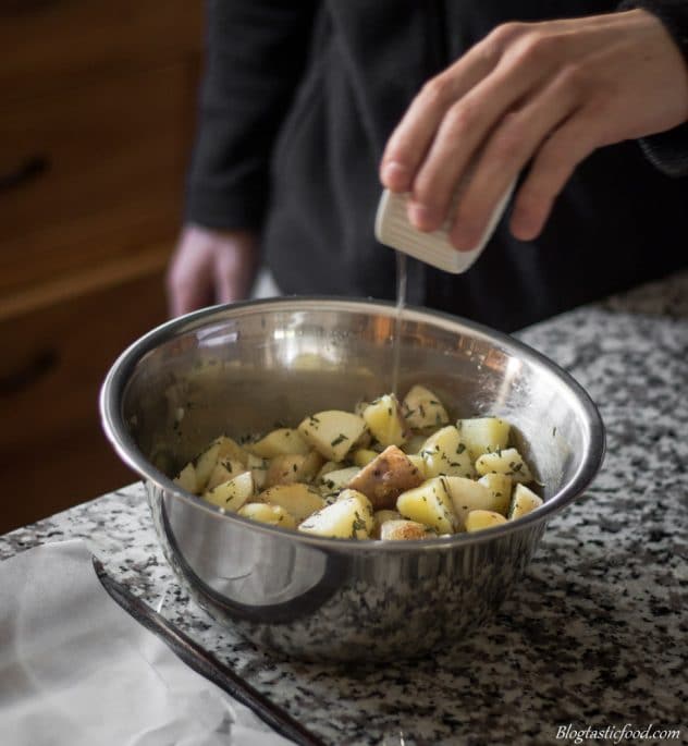 A photo of someone adding oil to a bowl of par-boiled potatoes.