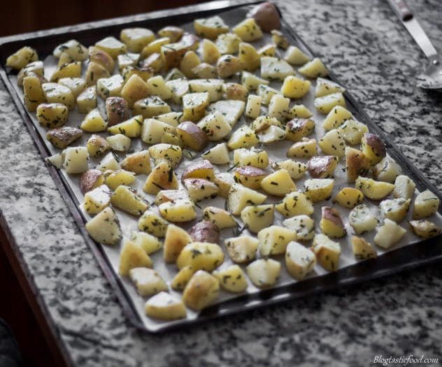 A photo of potatoes that are ready to be roasted spread out on a tray.