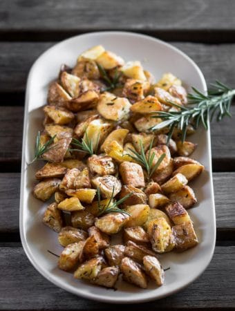 A picture of roasted potatoes and rosemary sprig served on a grey plate.