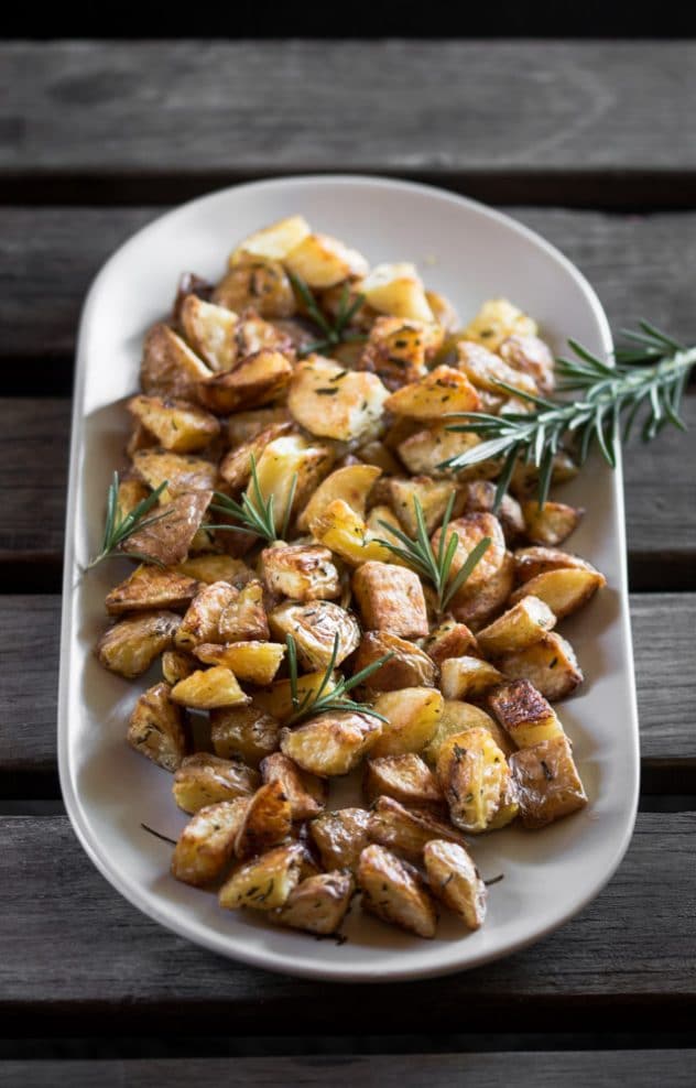 A picture of roasted potatoes and rosemary sprig served on a grey plate. 