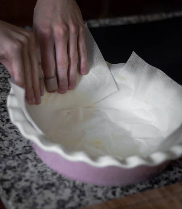 2 hands lining a pie dish with baking paper. 