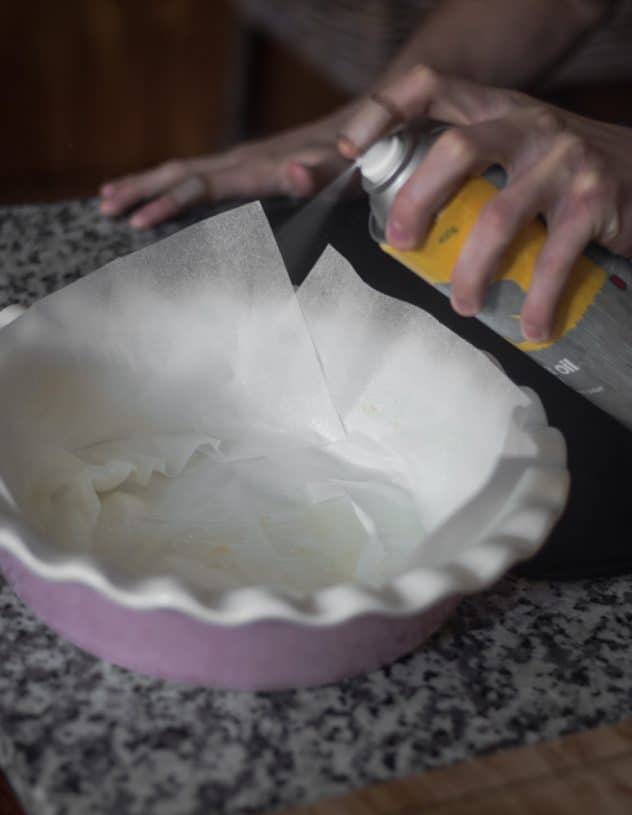 A person spraying baking paper on a pie dish with cooking spray. 
