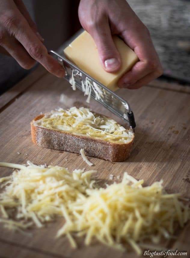 Cheese being grated over a slice of buttered bread.