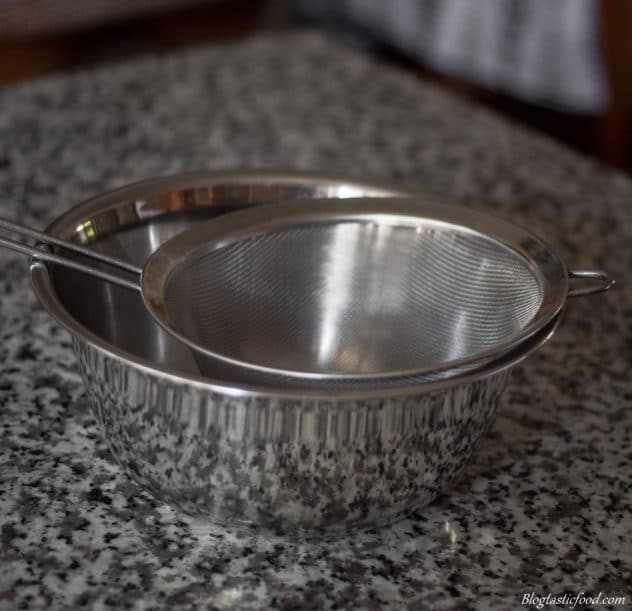 A photo of a sieve over a metal bowl.