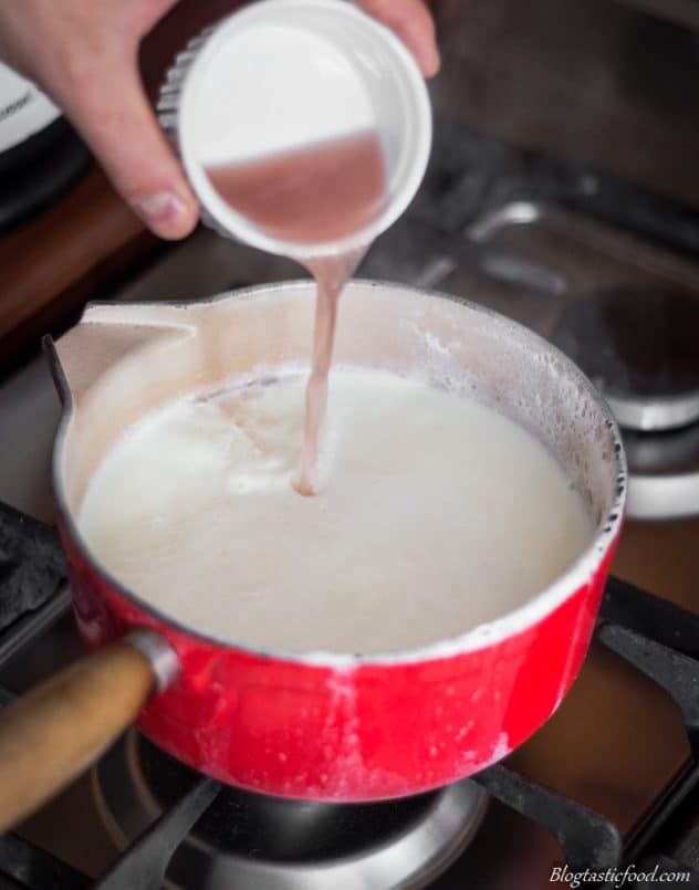 A photo of someone adding vinegar to a pot of hot milk.