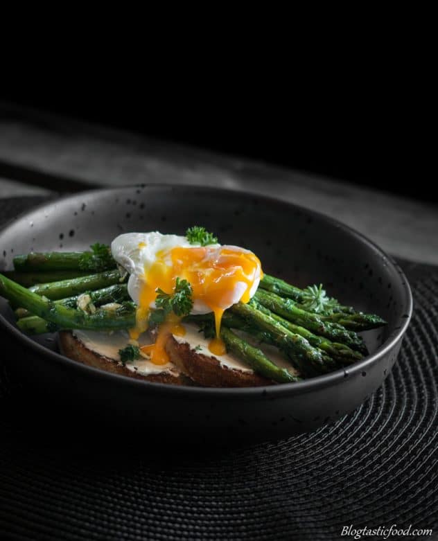 The yolk of a poached egg that has been busted over asparagus and cream cheese on toast.