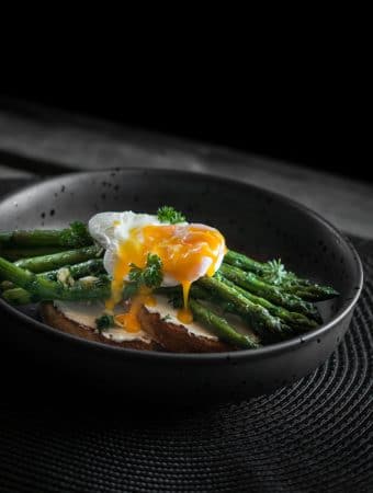 A photo of a poached egg with the yolk broken over asparagus and toast.