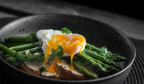 A photo of a poached egg with the yolk broken over asparagus and toast.