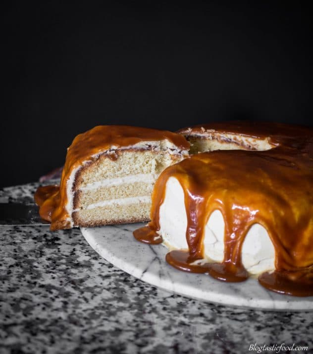 A photo of someone removing a portion out of a 3 layered salted caramel and baileys frosting cake.