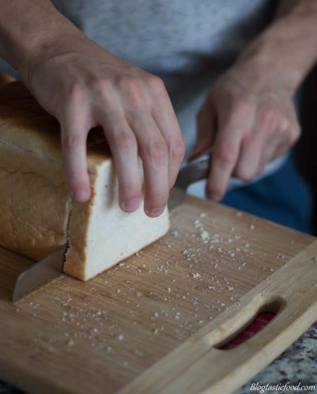A photo of someone using a serrated knife to cut into a loaf of white bread.