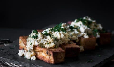 A dark, moody photo of French toast with scrambled eggs served on top.