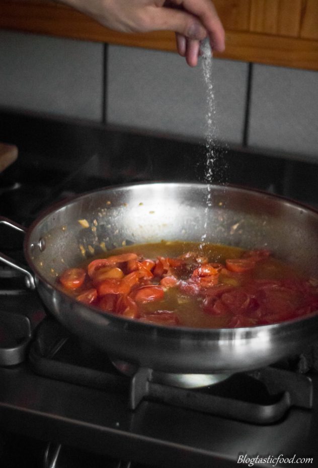 A photo of someone adding a pinch of sugar to tomato sauce.