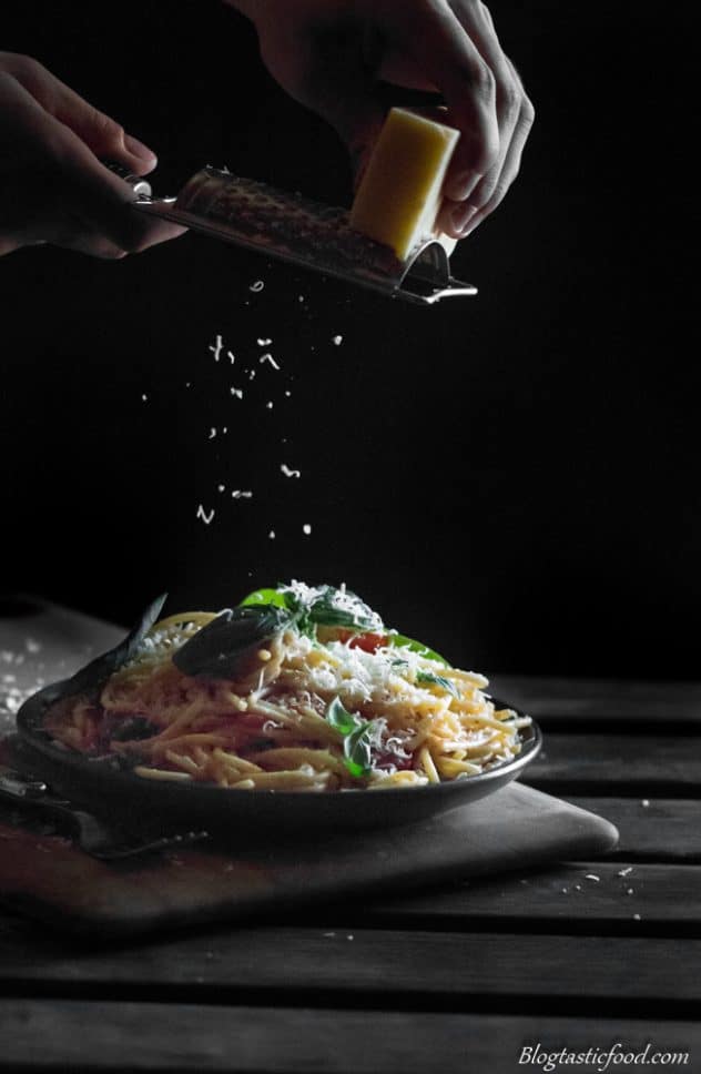 A photo of someone grating over some parmesan cheese over a plate of spaghetti.