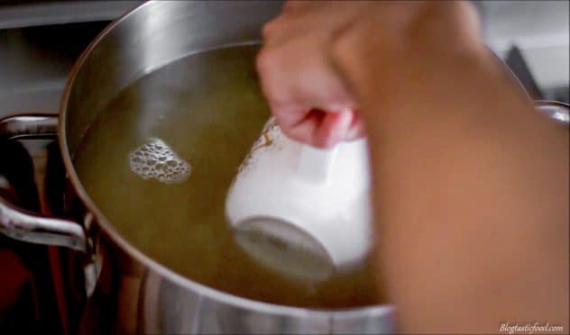 A photo of someone using a cup to scoop up some of the water that has been used to boil pasta.