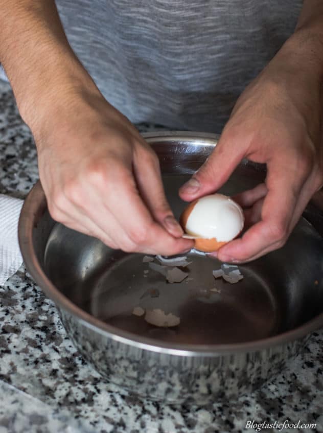 A photo of someone peeled a boiled egg over a bowl of cold water.