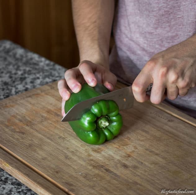 A photo of someone slicing the top of the bell pepper using a knife.
