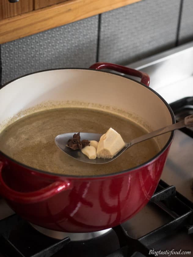 A photo of fresh ginger, fresh garlic and star anise being plunged into simmering stock.