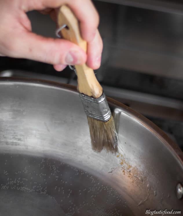 A photo of someone brushing water round the sides of a pan, to stop the sugar from crystallizing then making caramel.