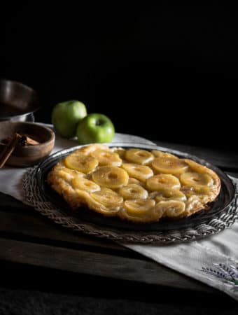 A photo of a tarte tatin with apples and cinnamon cloves in the background.