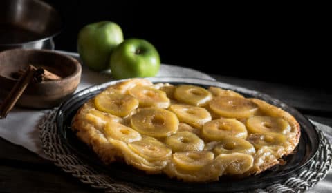 A photo of a tarte tatin with apples and cinnamon cloves in the background.