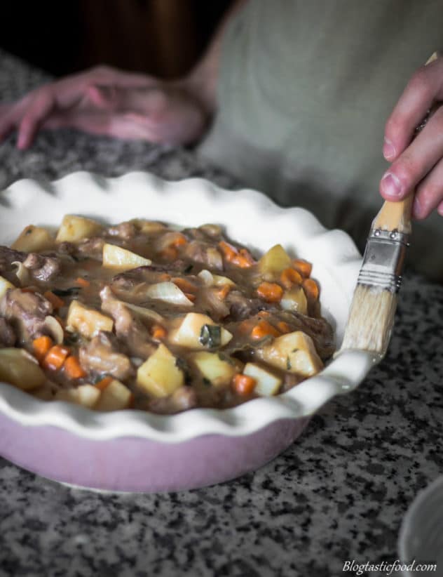 Egg wash being brushed around the rim of a pie dish.