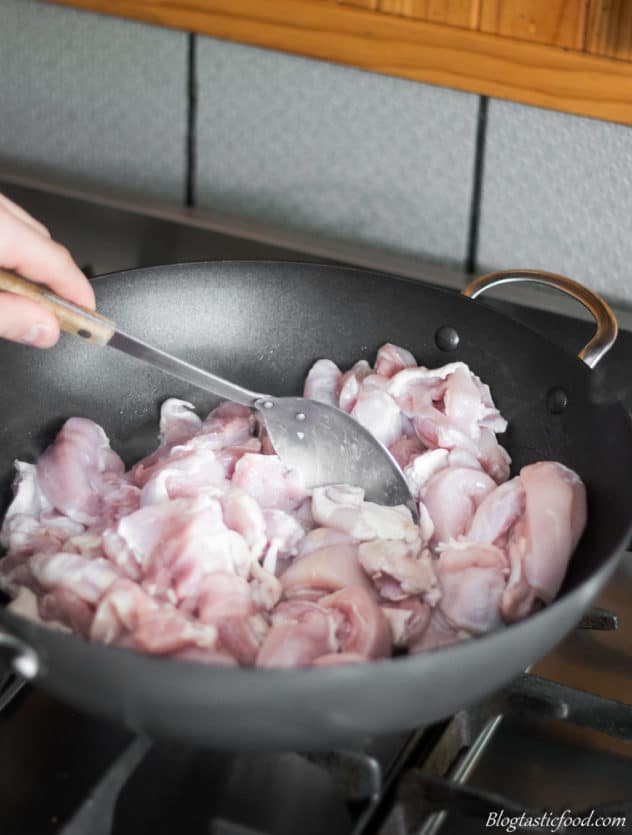 A photo of chicken getting fried in a wok.