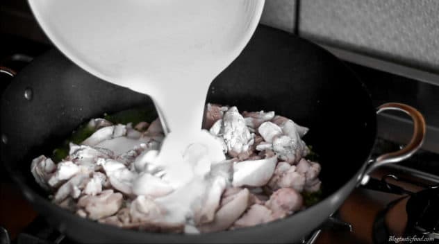A photo of someone adding coconut milk to a wok filled with chicken.