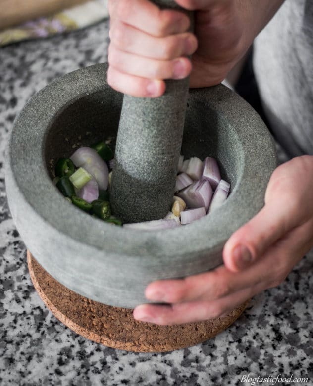 A photo of shallots, galangal, lemongrass, garlic and chillies getting bashed in a pestle mortar.