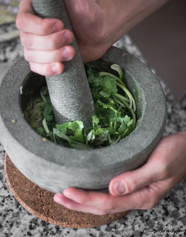 A photo of coriander and Thai basil getting bashed in pestle mortar.